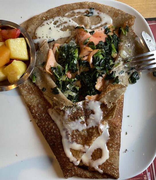Salmon and Spinach Galette on a plate, a fork showing the filling. Fruit cup to the left.